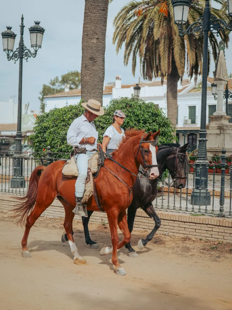Dos visitantes a caballo en una calle de arena de El Rocío