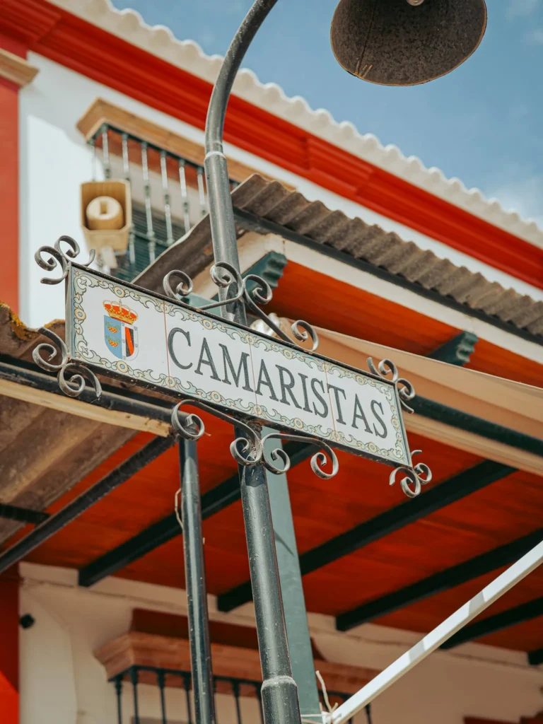 Rótulo Camaristas en un soporte de hierro forjado junto a una fachada blanca de El Rocío