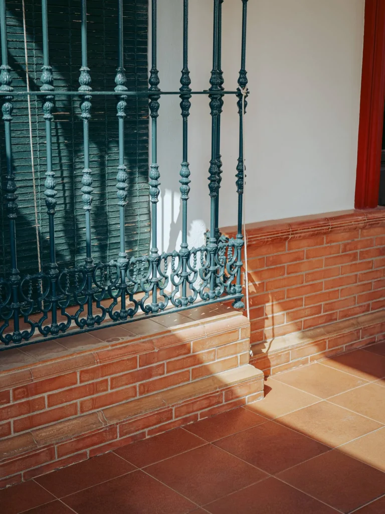 Reja de ventana, ladrillos rojos y sombras en una fachada blanca de El Rocío
