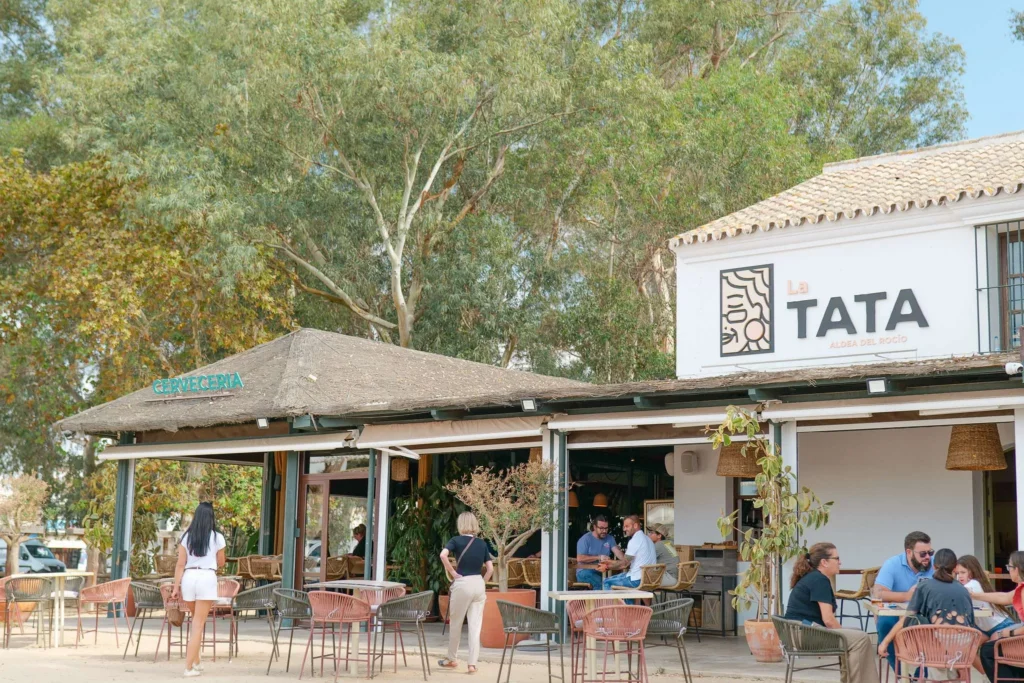 Terraza de La Tata en El Rocío con comensales, árboles y el rótulo del restaurante
