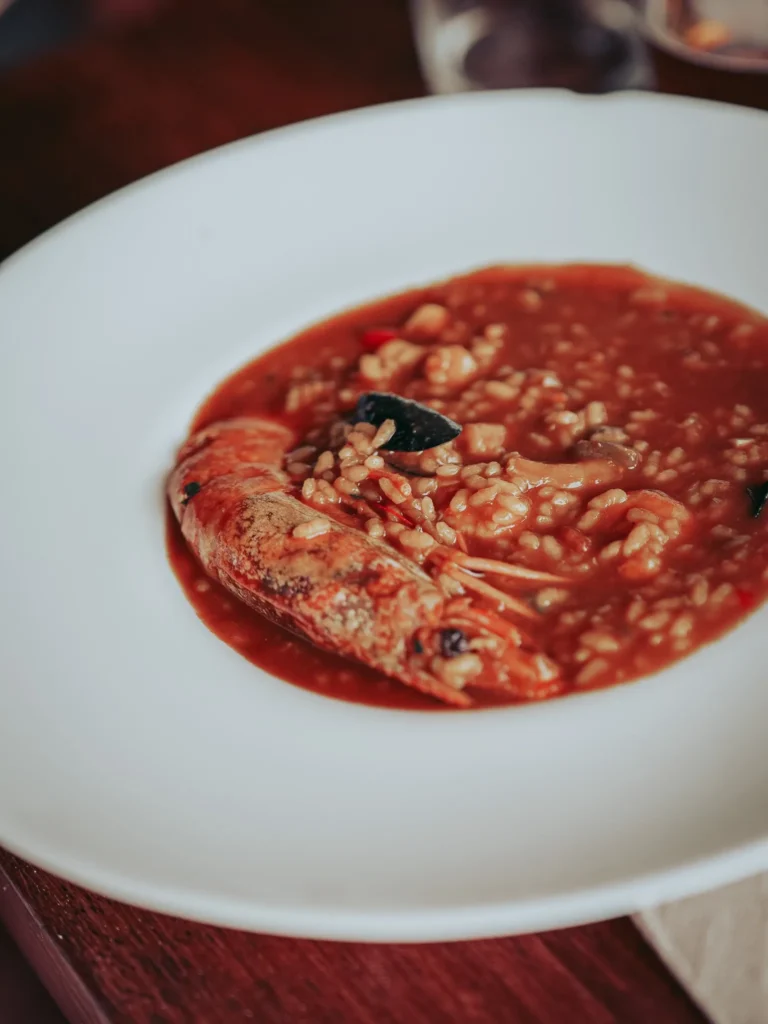 Plato hondo de arroz de marisco con caldo rojo y un langostino en La Tata